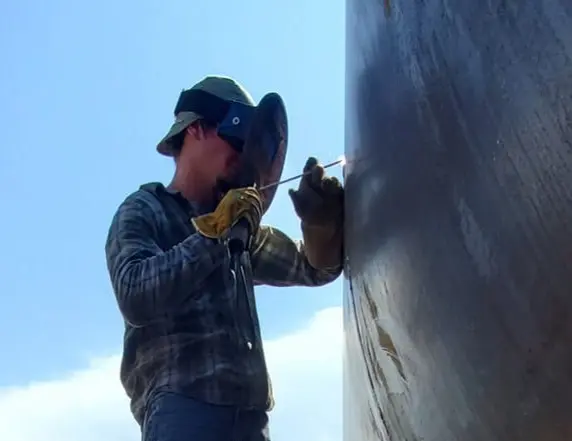 This image is of a welder repairing a seam on a large container tank.