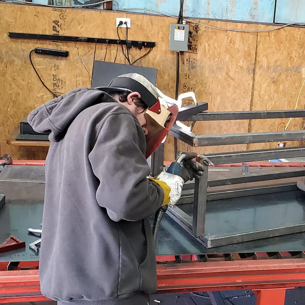 This image shows a welder in the BWF shop working on a box frame.